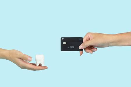 A hand holding a tooth and a hand holding a credit card